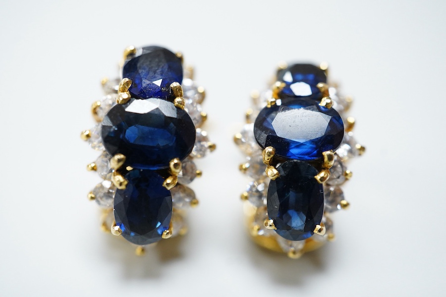A pair of sapphire earrings, each set with three oval sapphires, within a border of brilliant-cut cubic zirconias, mounted in gold, length 1.4cm each, clip and retractable post fittings